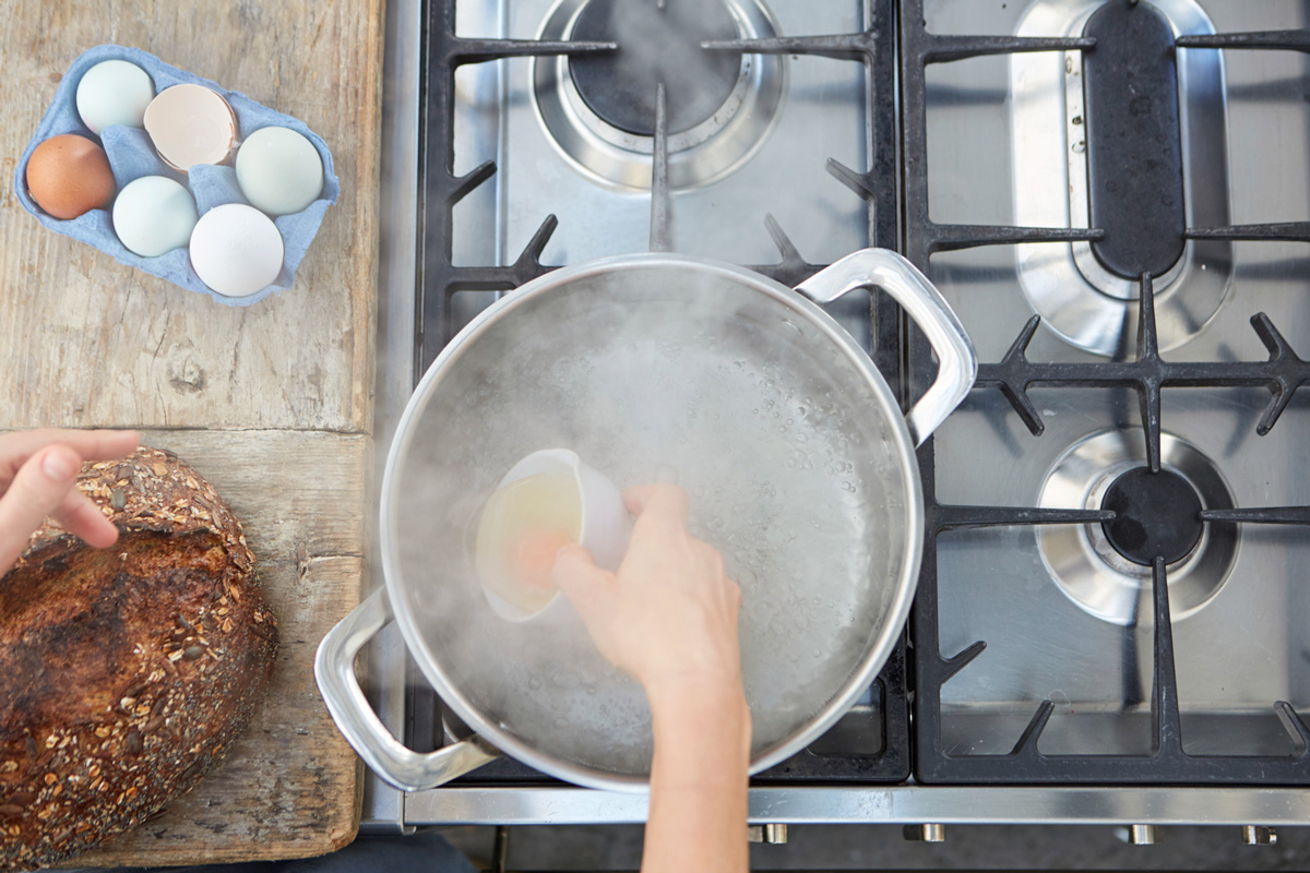 Image of an egg being poured into the pan of boiling water