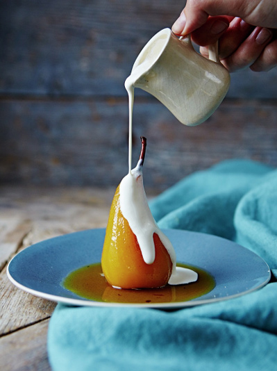 cream being poured over a poached pear